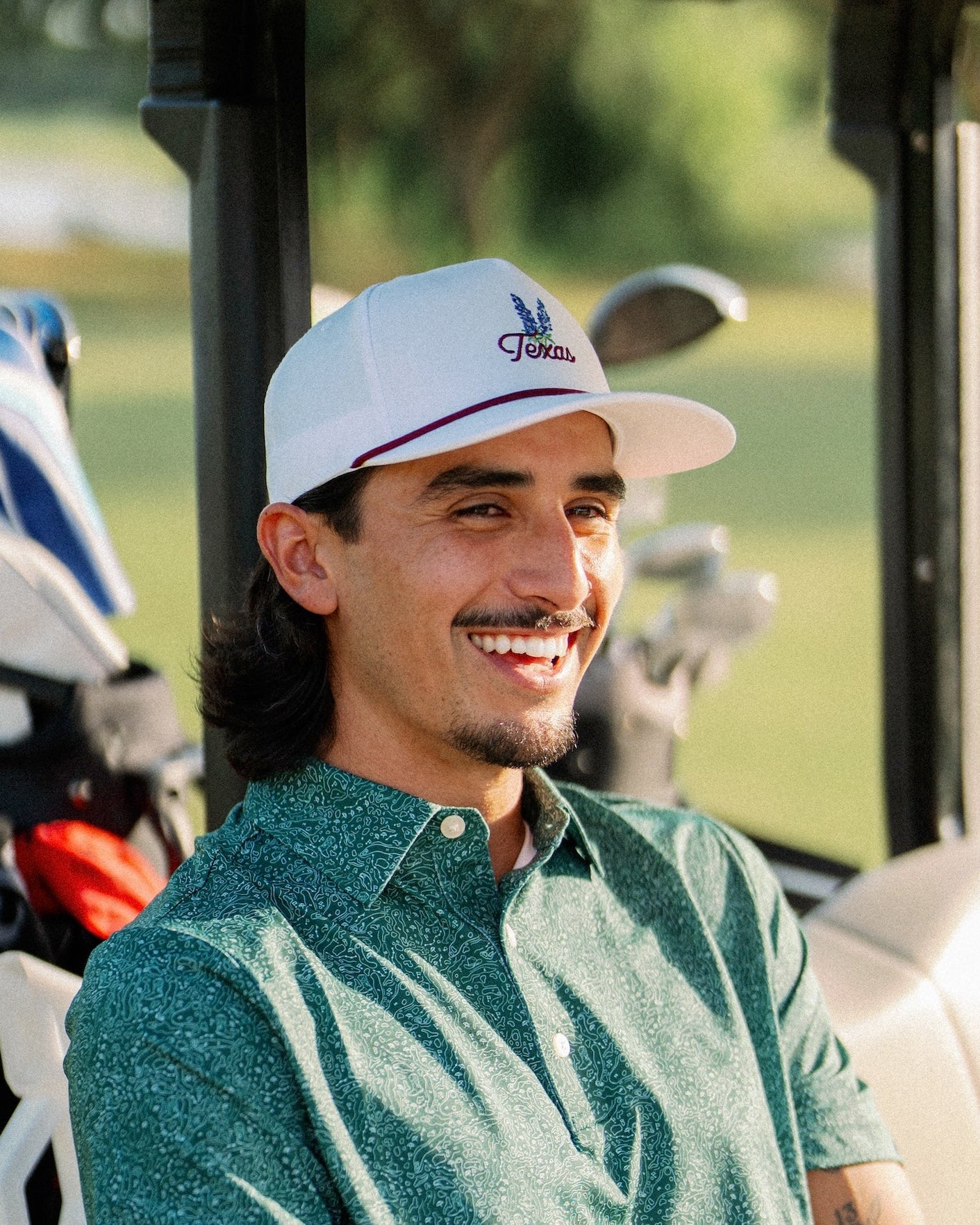 Smiling golfer wearing the Texas Bluebonnet Maroon Rope Hat in a golf cart