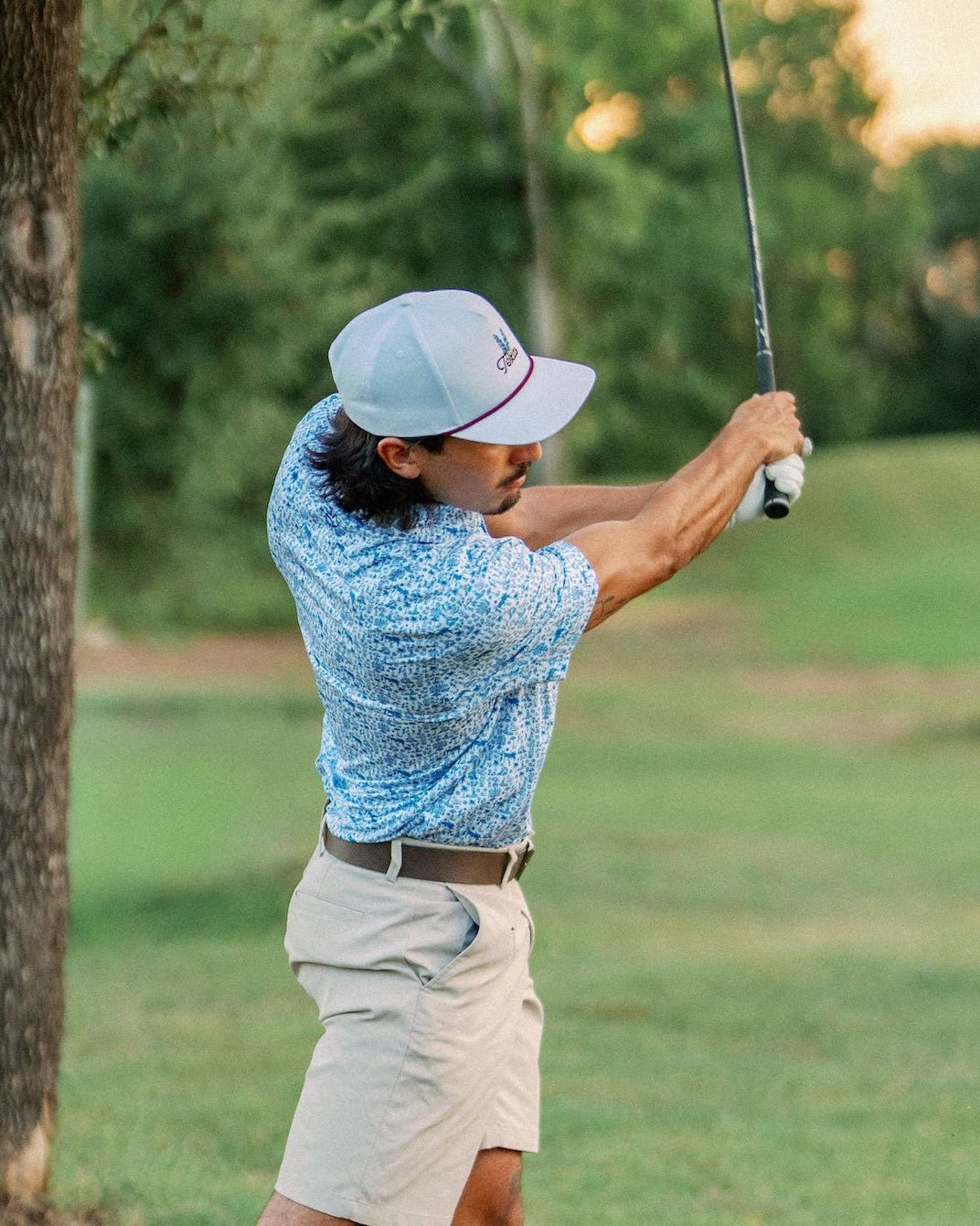 Golfer finishing his swing at golden hour in the Texas Bluebonnet Maroon Rope Hat