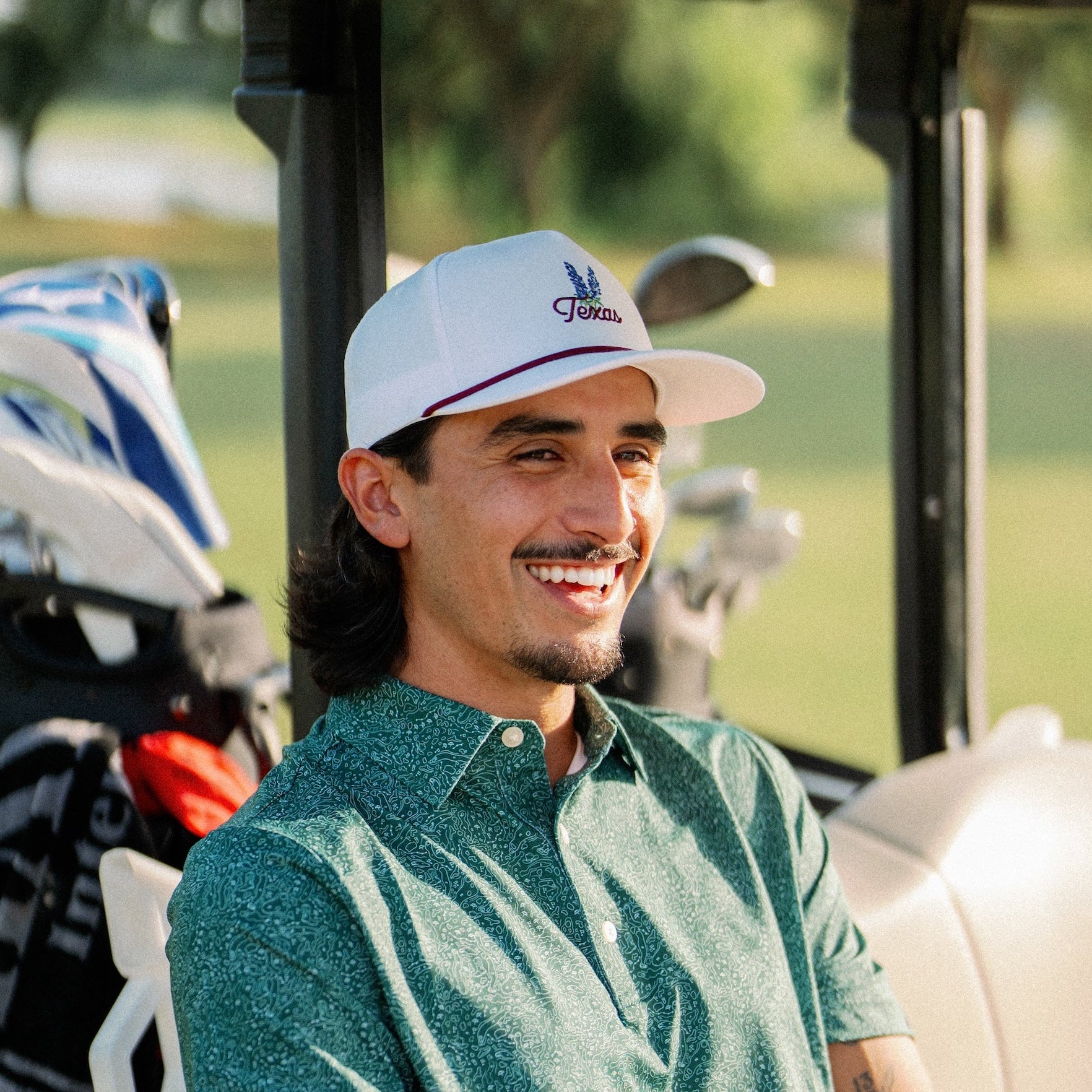 Smiling golfer wearing the Texas Bluebonnet Maroon Rope Hat in a golf cart