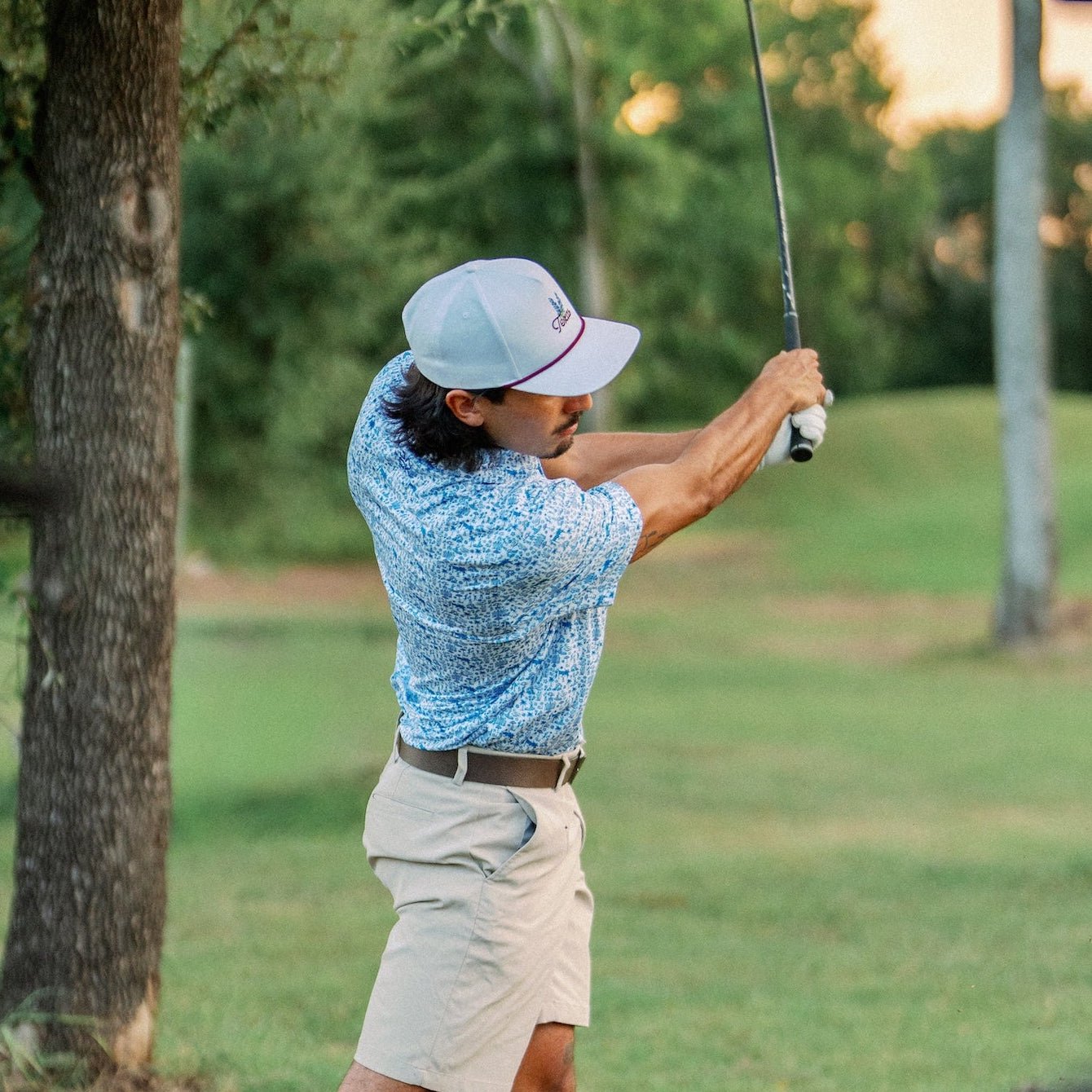 Golfer finishing his swing at golden hour in the Texas Bluebonnet Maroon Rope Hat